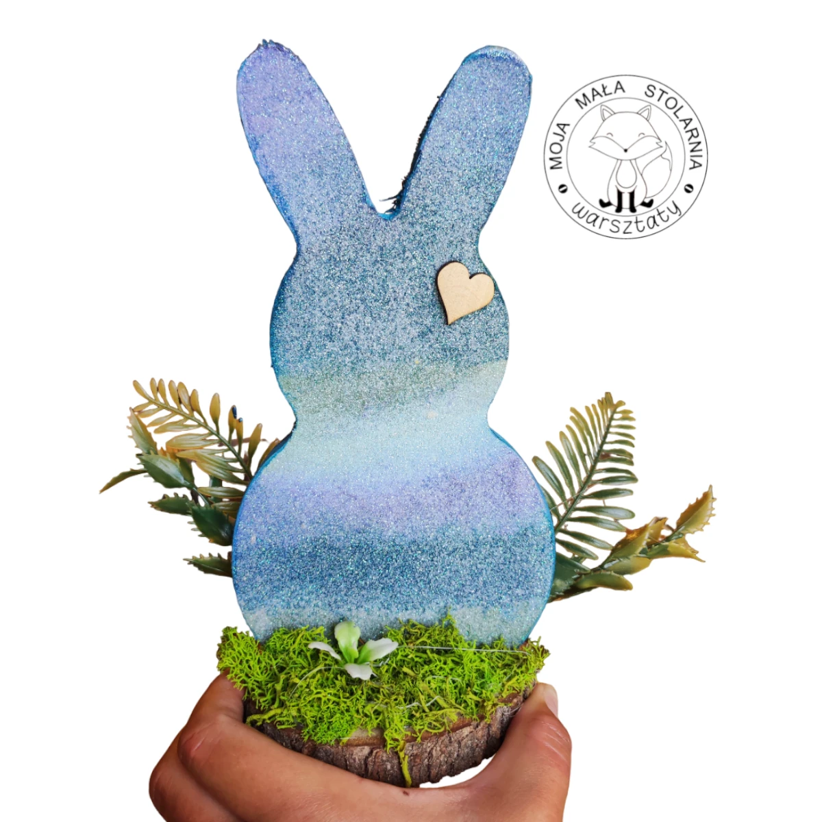 drewniany zajączek na plastrze drewna upstrzony mchem chrobotkiem i kolorowymi kwiatami, pomalowany w paski ombre